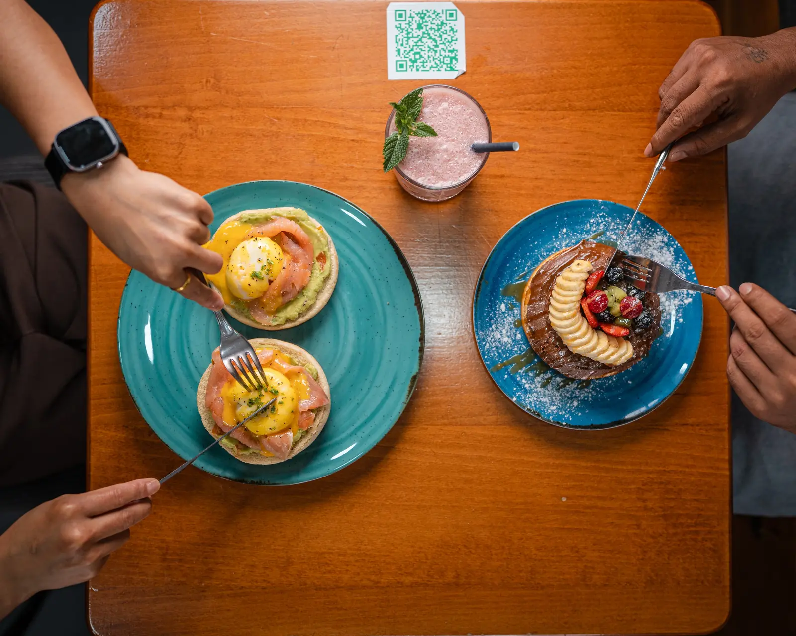 Two guests sharing eggs Benedict and Nutella pancakes at a wooden table